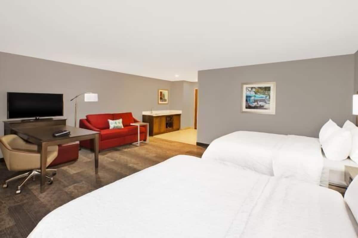 A hotel room with a bed, a desk, a red sofa, a TV, and a painting on the wall.