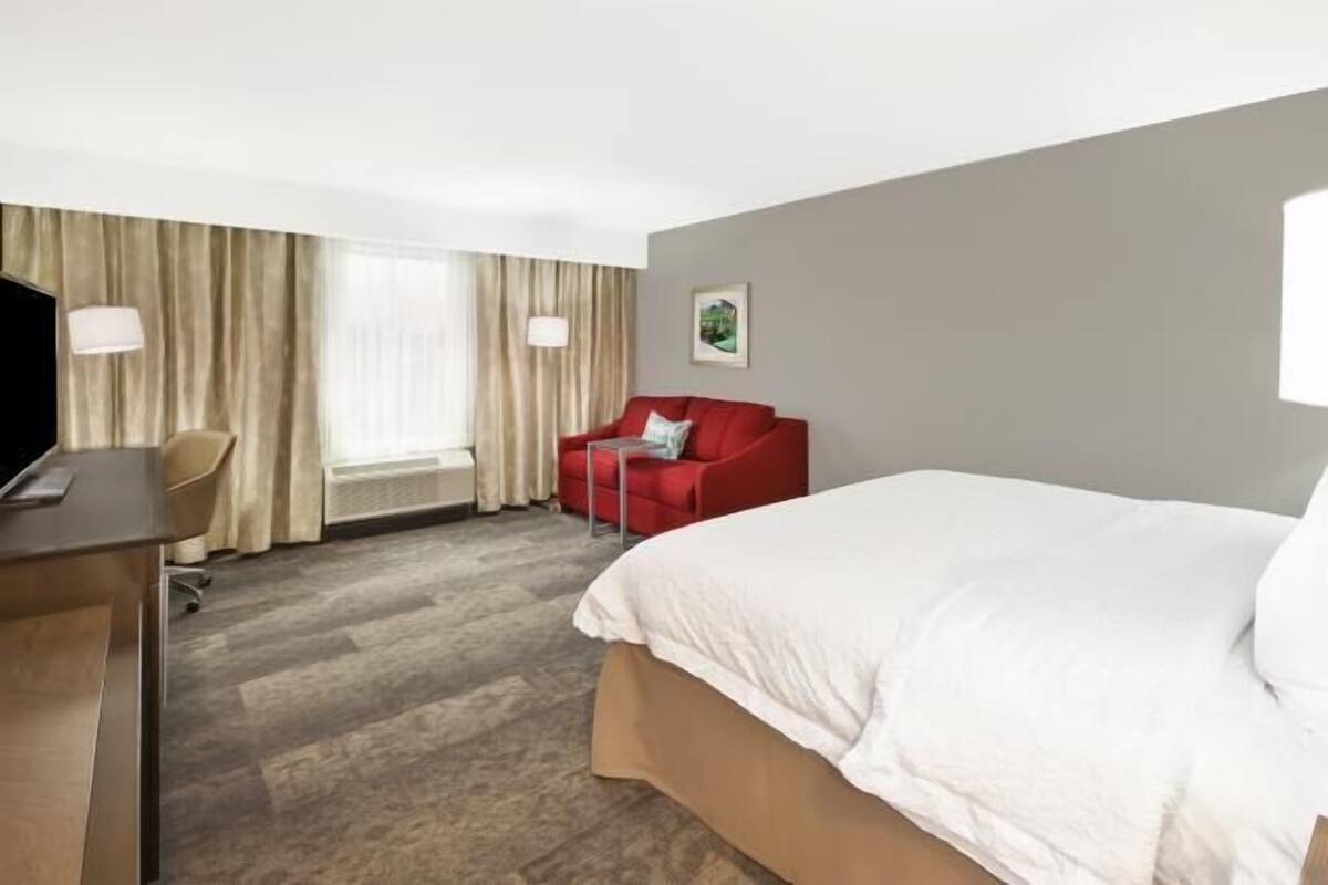 A hotel room with a bed, a desk, a chair, and a TV.