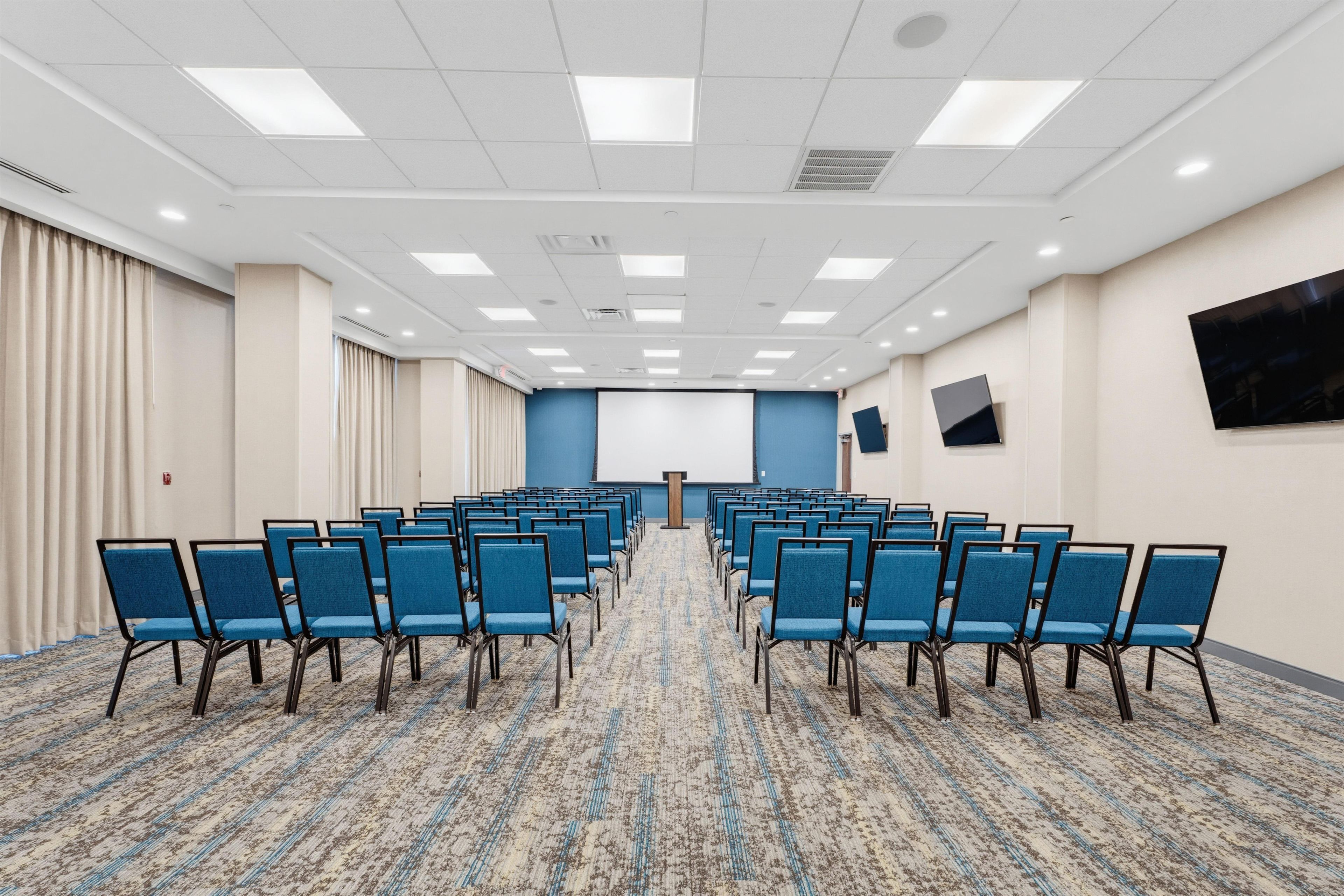 A conference room with rows of chairs, a podium, and a large screen on the wall.