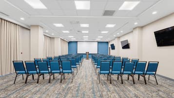 A conference room with rows of chairs, a podium, and a large screen on the wall.