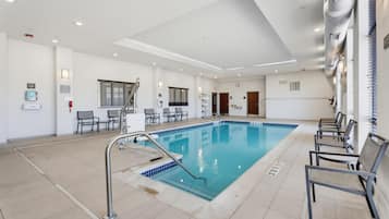 Una piscina con borde de baldosas, rodeada de sillas y una escalera que sube a niveles superiores.