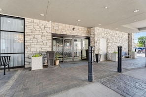 A building entrance with a stone facade, a glass door, and a welcome mat. - Hampton Inn by Hilton Detroit Dearborn (Dearborn)