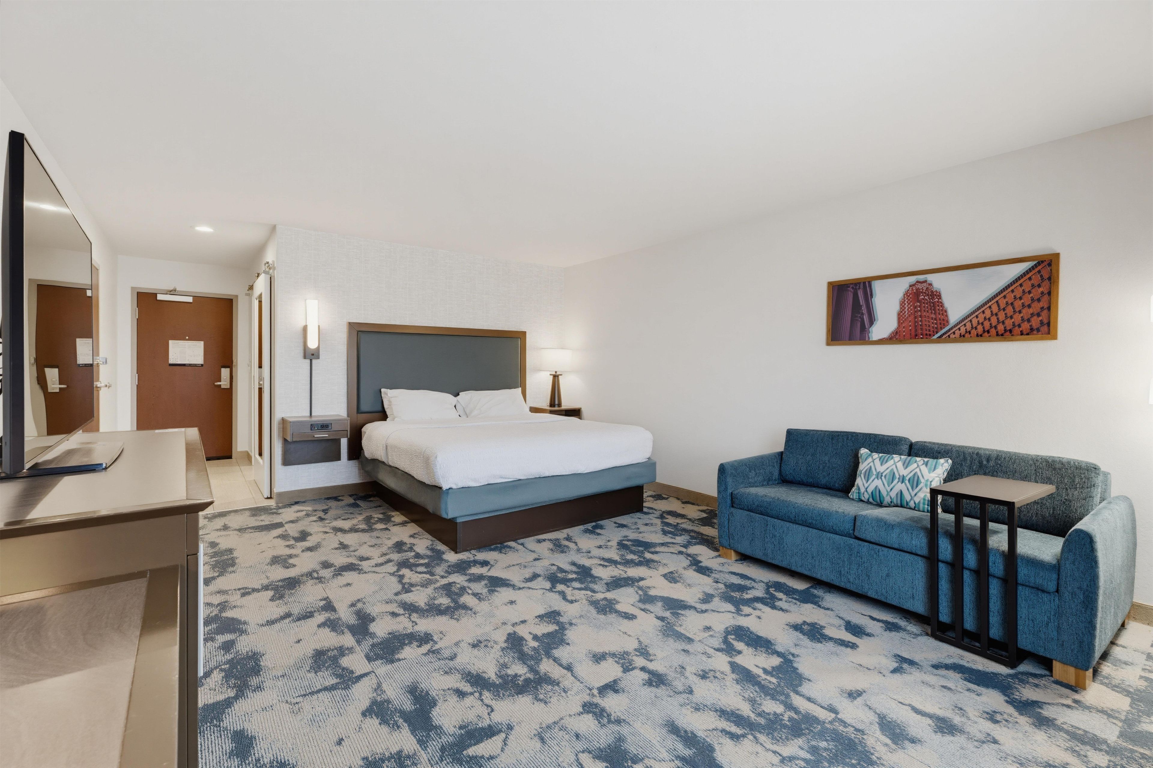 A hotel room with a bed, a sofa, a desk, and a television.