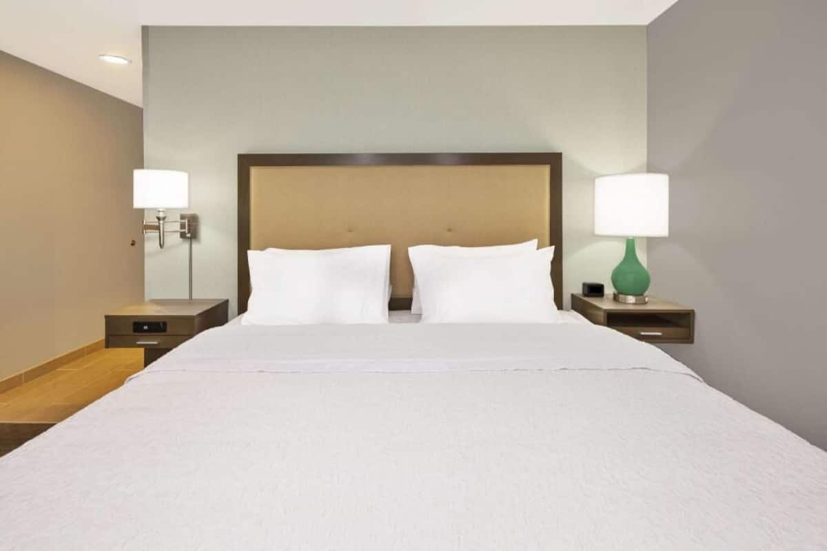 A hotel room with a large bed, two bedside tables, and two wall-mounted lamps.