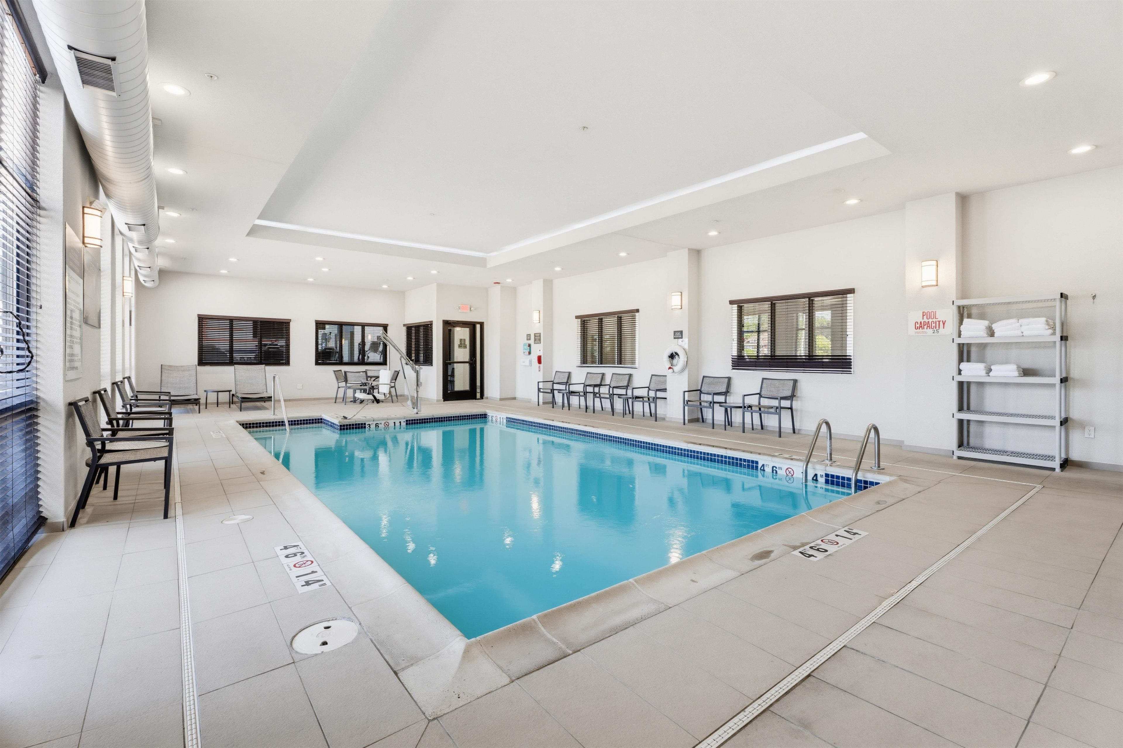 Una piscina interior limpia con marcas claras de carriles, un vestuario con ducha y una zona de estar con sillas.