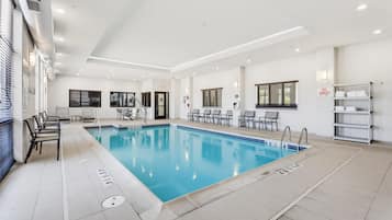 Una piscina interior limpia con marcas claras de carriles, un vestuario con ducha y una zona de estar con sillas.