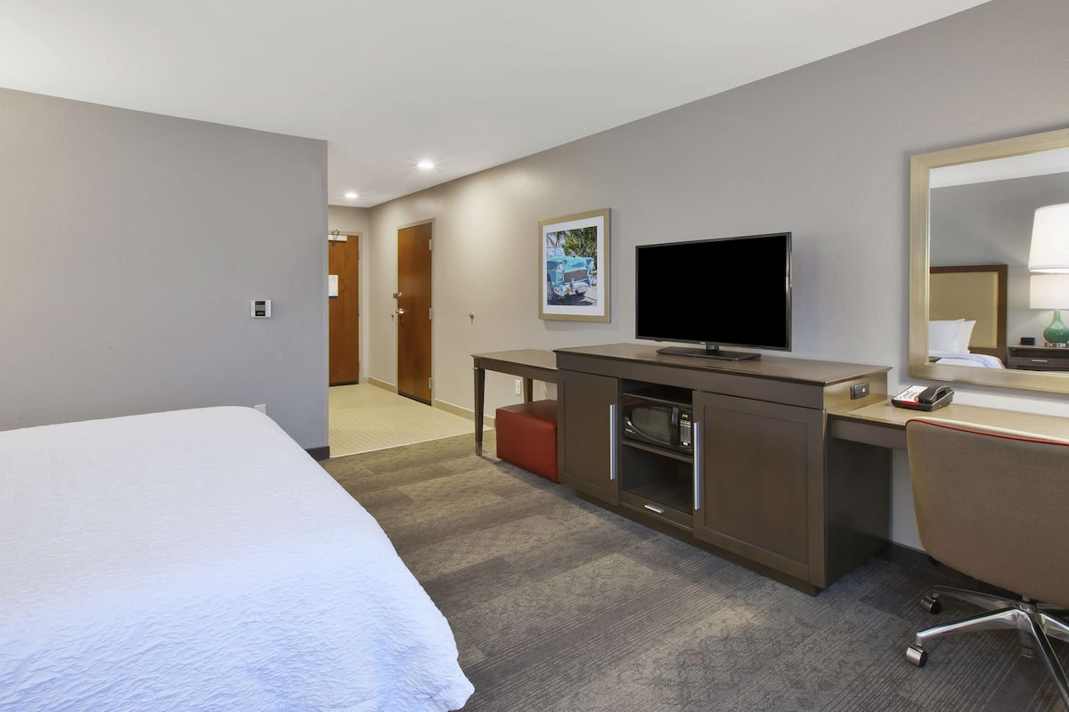 A hotel room with a large bed, a desk with a flat-screen TV, a microwave, and a telephone.