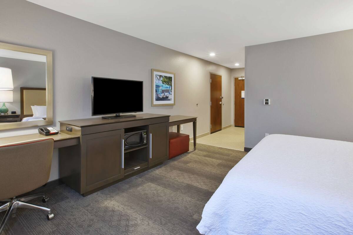 A hotel room with a bed, a desk with a television, a telephone, and a framed picture on the wall.