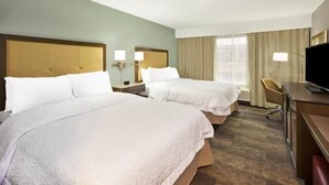 A hotel room with two beds, a desk, a chair, and a television.