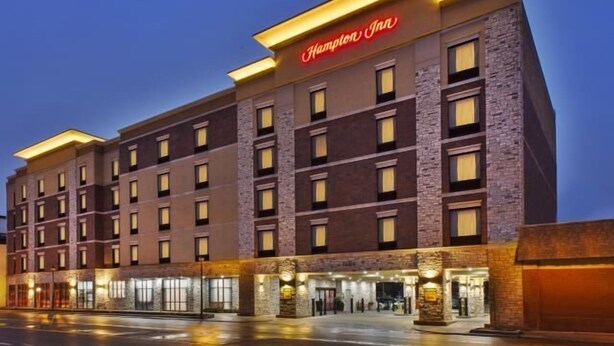 A Hampton Inn hotel with a modern design, featuring multiple floors and a prominent entrance with illuminated signage.