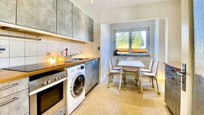 A modern kitchen with a built-in oven, washing machine, and a dining area with a table and chairs. - Apartment Avanzato (Erfurt)