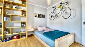Ein Schlafzimmer mit einem hölzernen Bett, einem Bücherregal, einem an der Wand befestigten Fahrrad und einem kleinen Schreibtisch mit Stuhl.