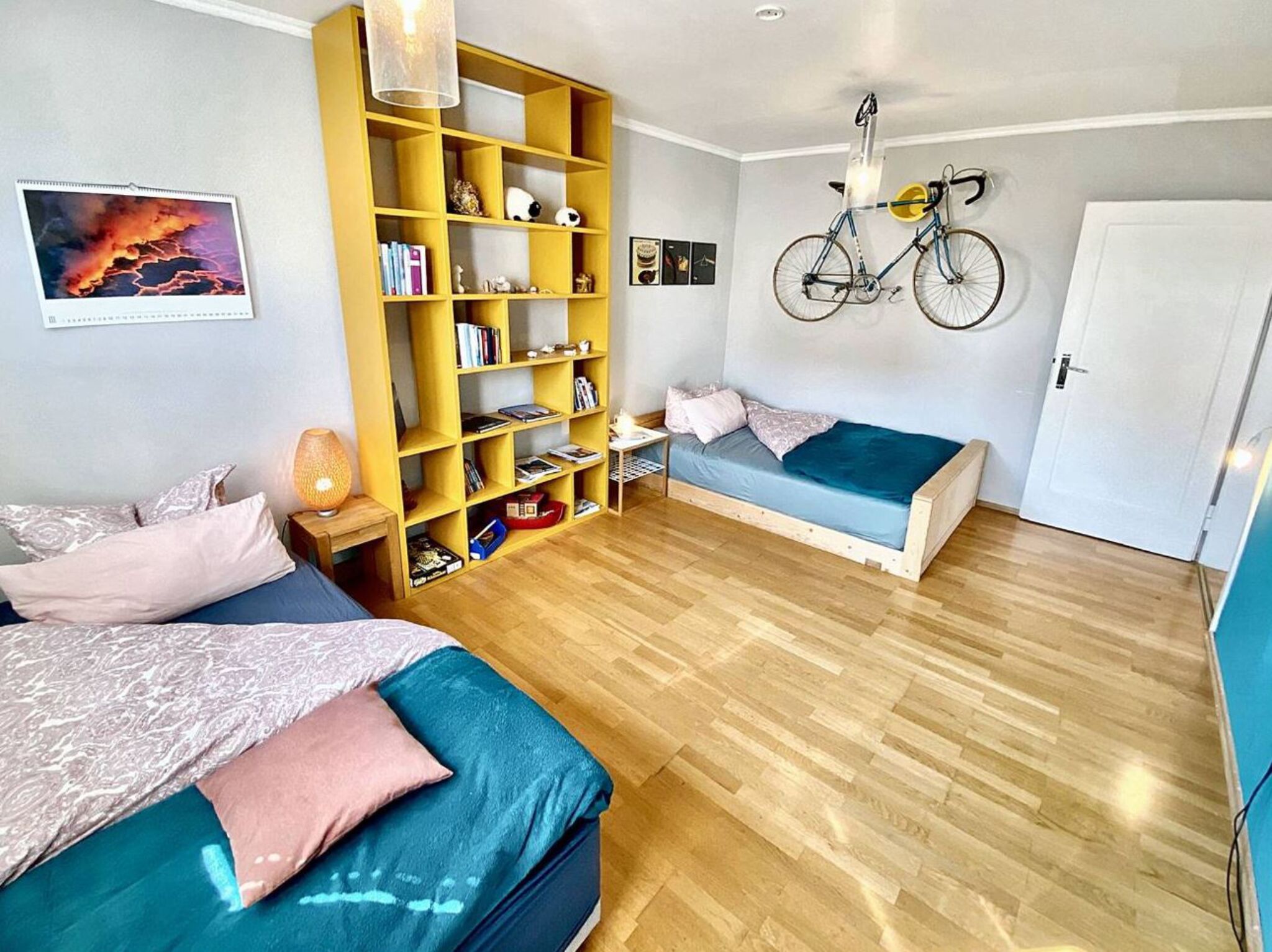 Ein Schlafzimmer mit zwei Betten, einem Bücherregal, einem Fahrrad und einer Tür.