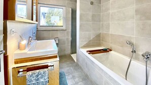 A modern bathroom with a bathtub, a sink, and a window. - Apartment Avanzato (Erfurt)