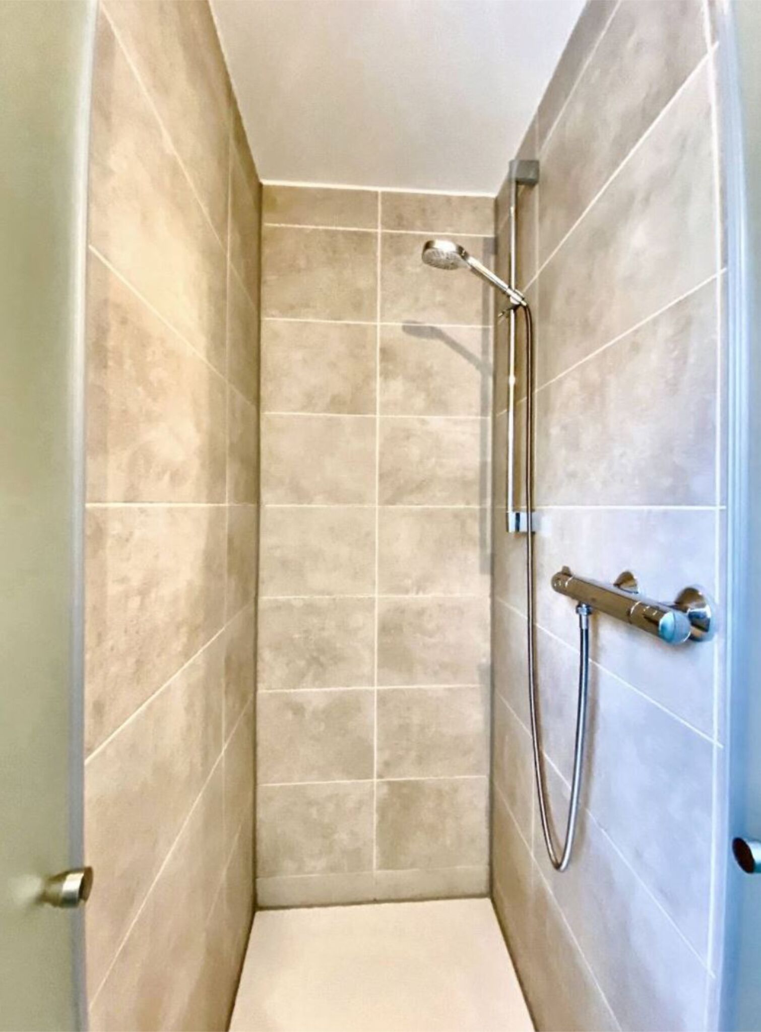 A small, tiled shower room with a handheld showerhead and a wall-mounted faucet.