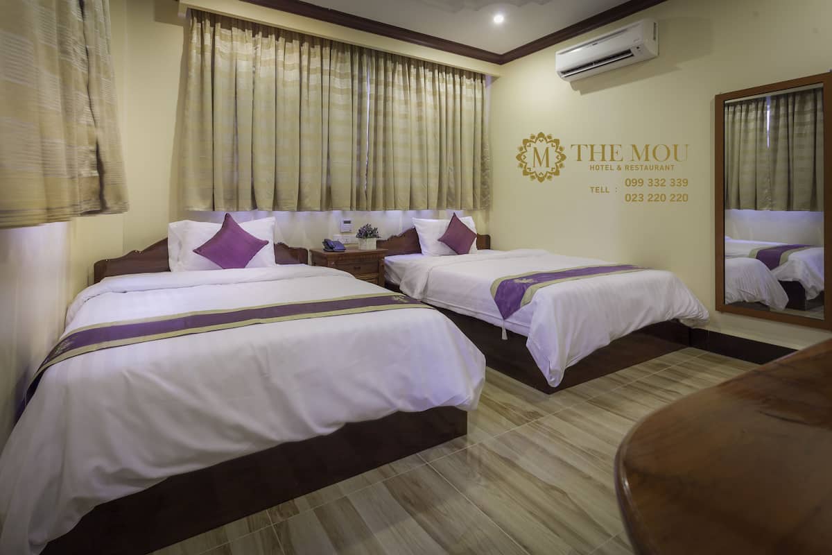 Habitación de hotel con dos camas, una mesita de noche, un espejo y un aire acondicionado de pared.