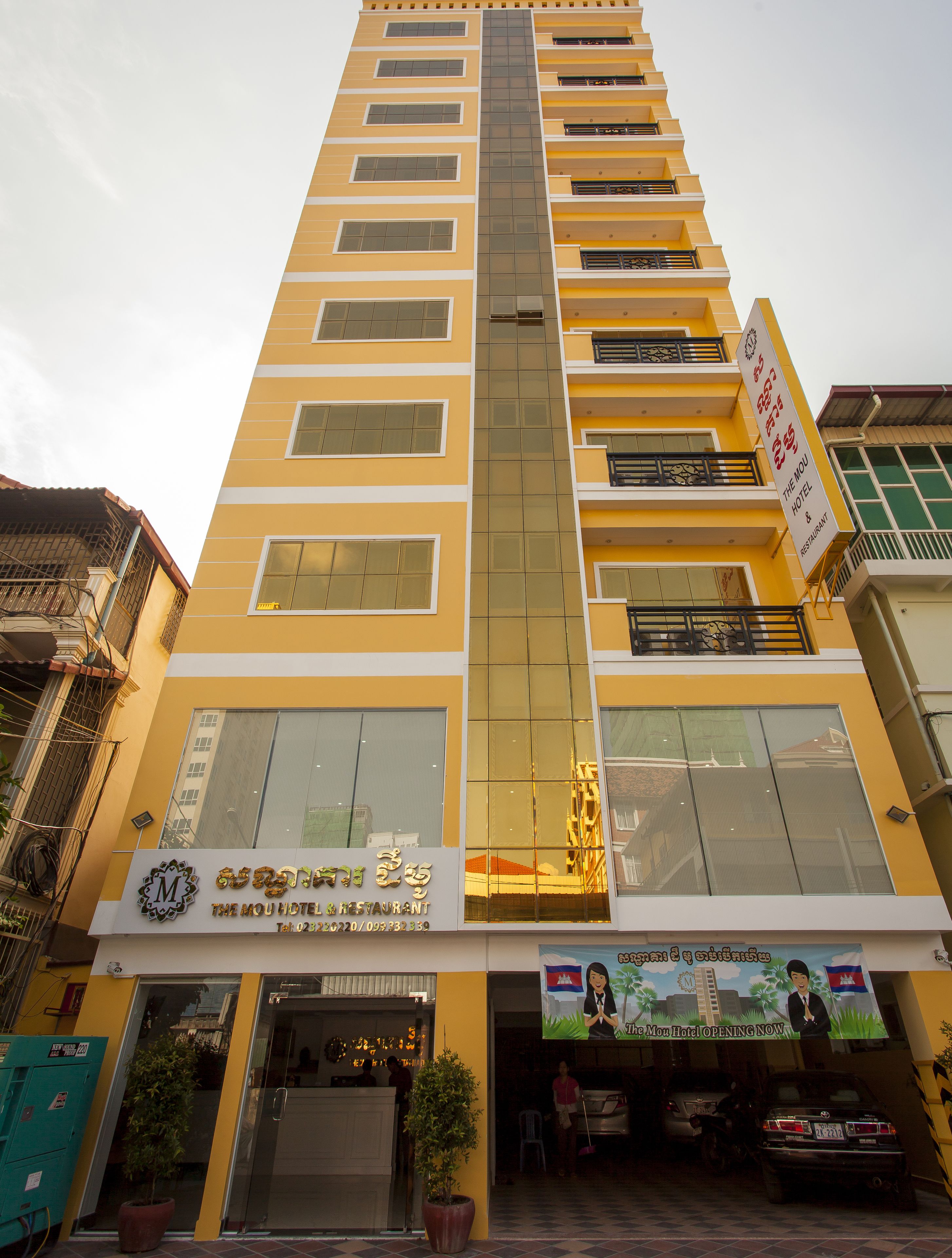 A multi-story hotel with a yellow facade, large windows, and a sign indicating it is the Mou Hotel & Restaurant.