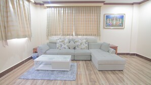 A living room with a sectional sofa, a coffee table, and a painting on the wall. - The Mou Hotel (Phnom Penh)