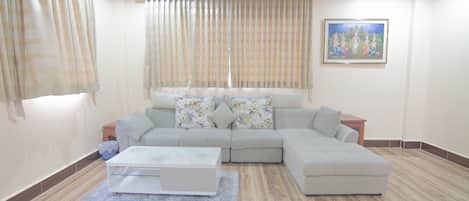 Uma sala de estar com sofá seccional, uma mesa de centro e um quadro na parede.