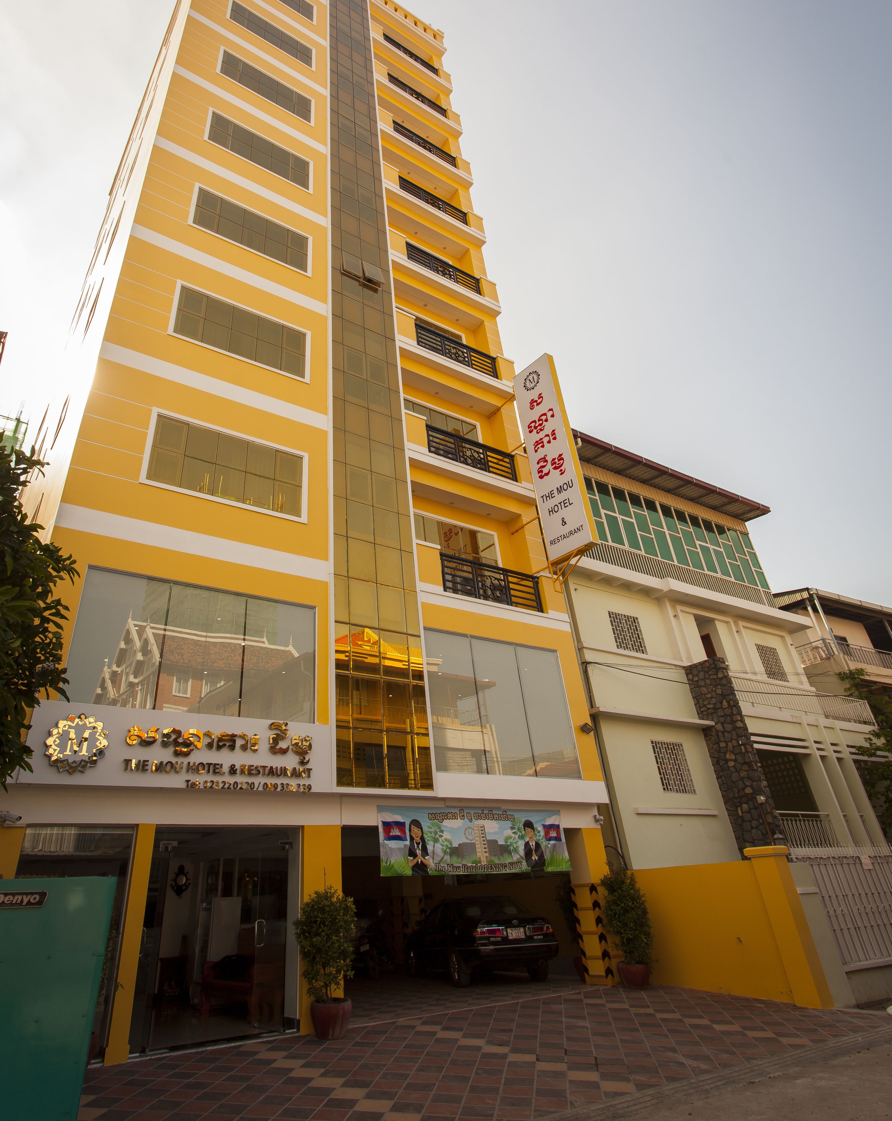 Ein mehrstöckiges Hotel mit gelber Fassade, Balkonen und einem Schild, das anzeigt, dass es sich um The Mou Hotel & Restaurant handelt.