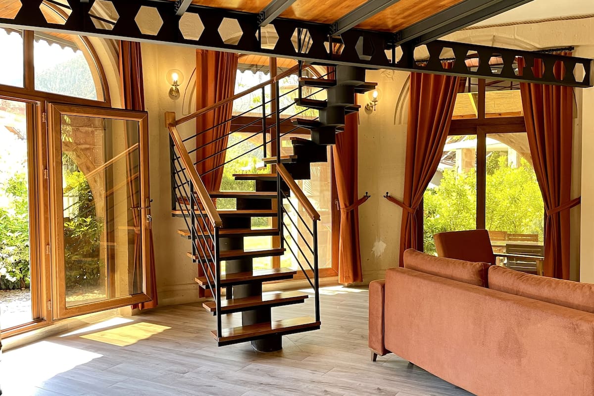 Un intérieur moderne avec un escalier en bois, un canapé et de grandes fenêtres donnant sur un paysage verdoyant.