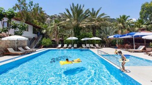 Una piscina con sillas de descanso y sombrillas, rodeada de palmeras y un edificio de fachada de piedra.