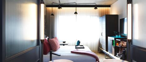 A modern hotel room with a large bed, two bedside tables, a TV, and a minibar.