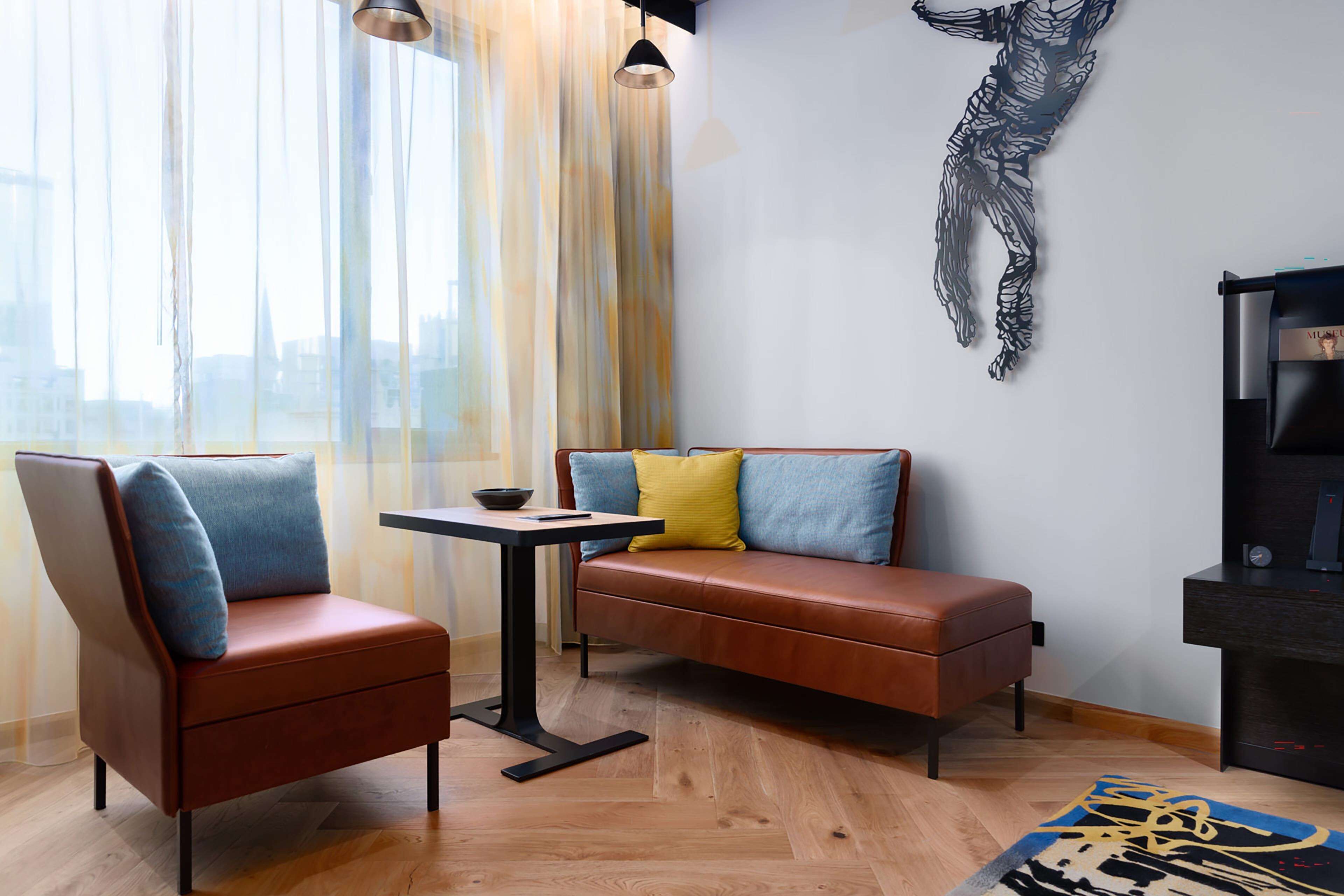 A modern living room with a brown leather sofa, two armchairs, a small table, and a decorative wall piece.