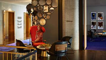Un vestíbulo moderno con una gran silla roja, una pared de espejos y una zona de comedor con una mesa y sillas.
