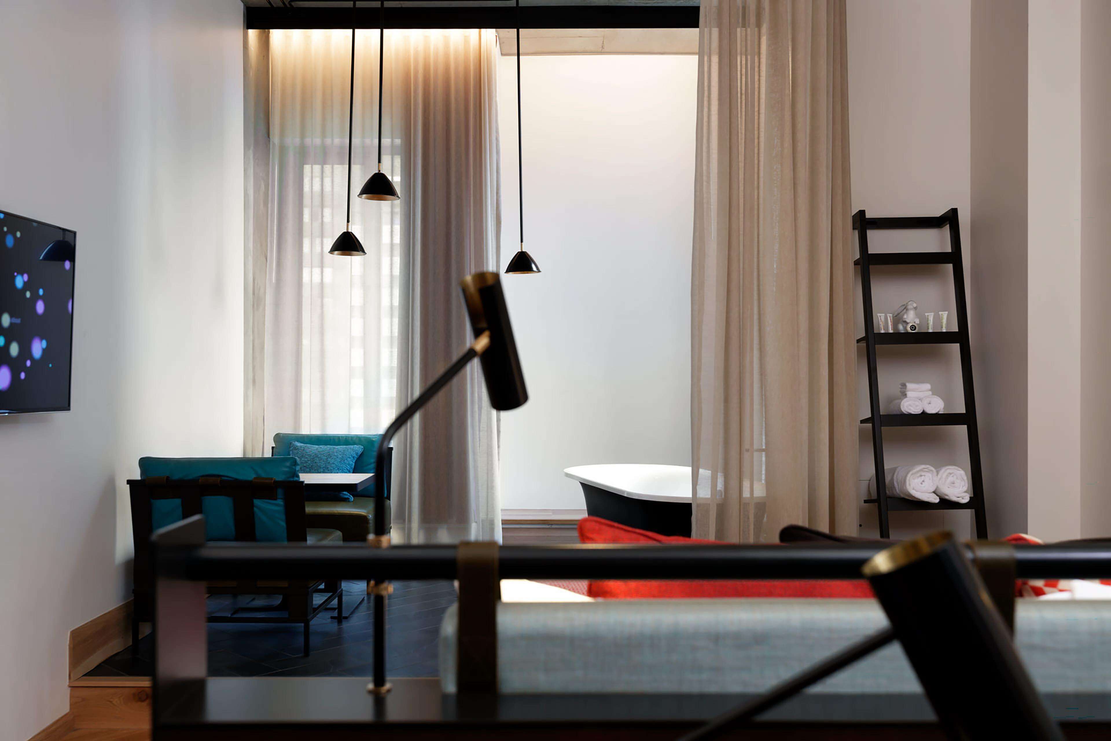 Una habitación de hotel moderna con una zona de comedor, un televisor y un estante negro con toallas.