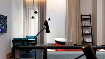 Una habitación de hotel moderna con una zona de comedor, un televisor y un estante negro con toallas.