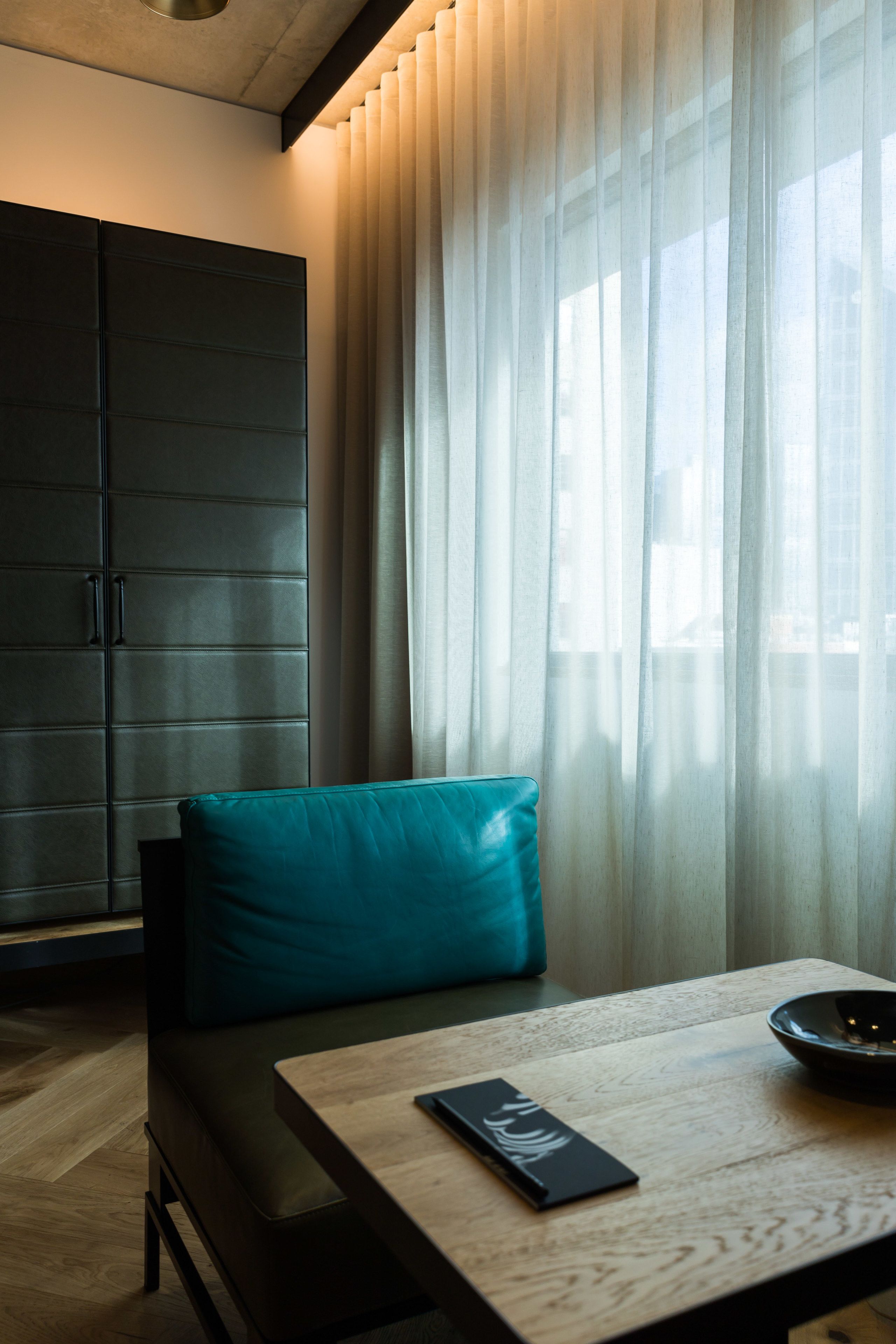 A modern room with a sofa, a wooden table, and a large window with sheer curtains.