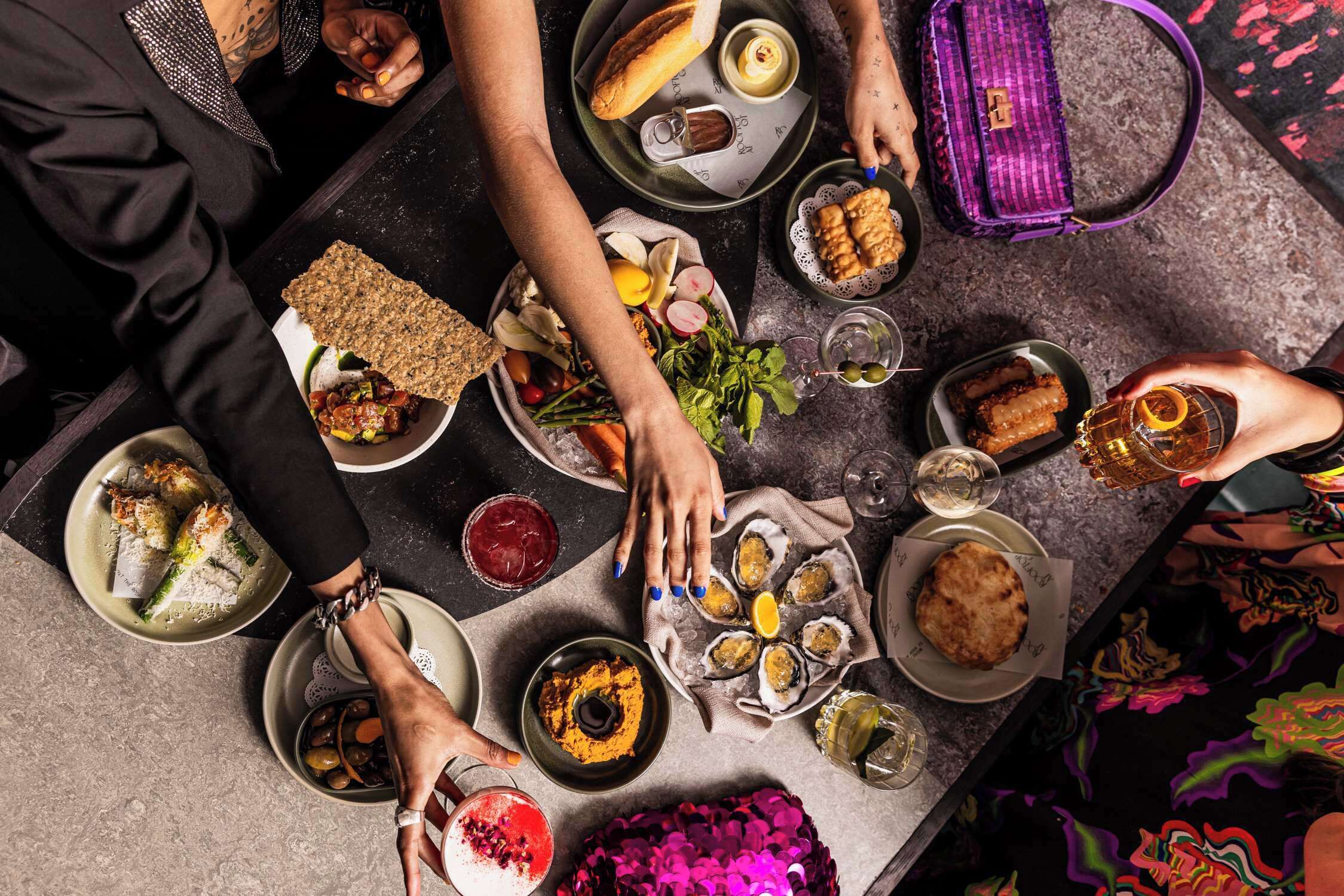 Un grupo de personas cenando en una mesa con diferentes platos, bebidas y un bolso morado.