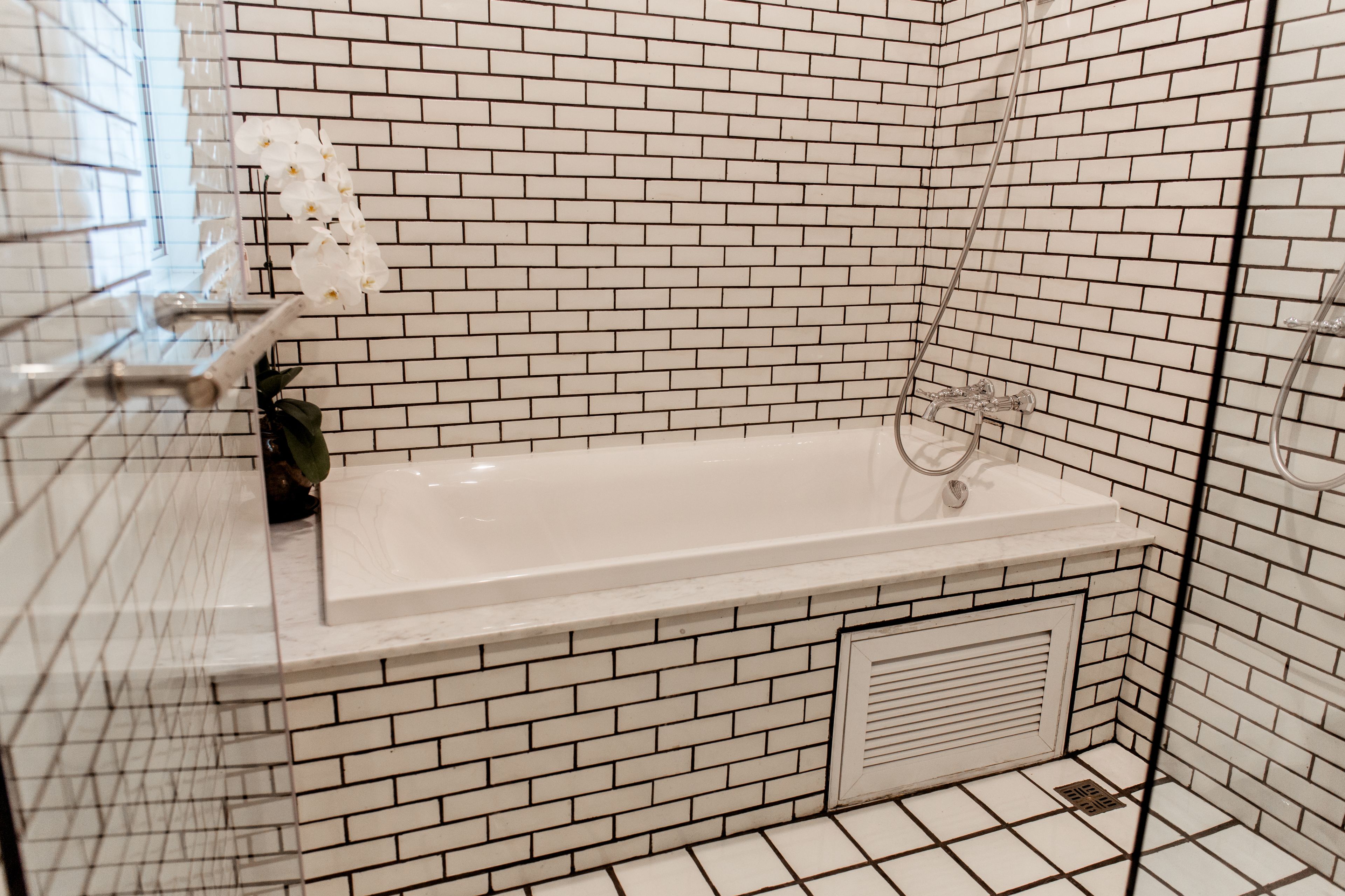 A bathroom with a white bathtub, white tiled walls, and a white tiled floor.