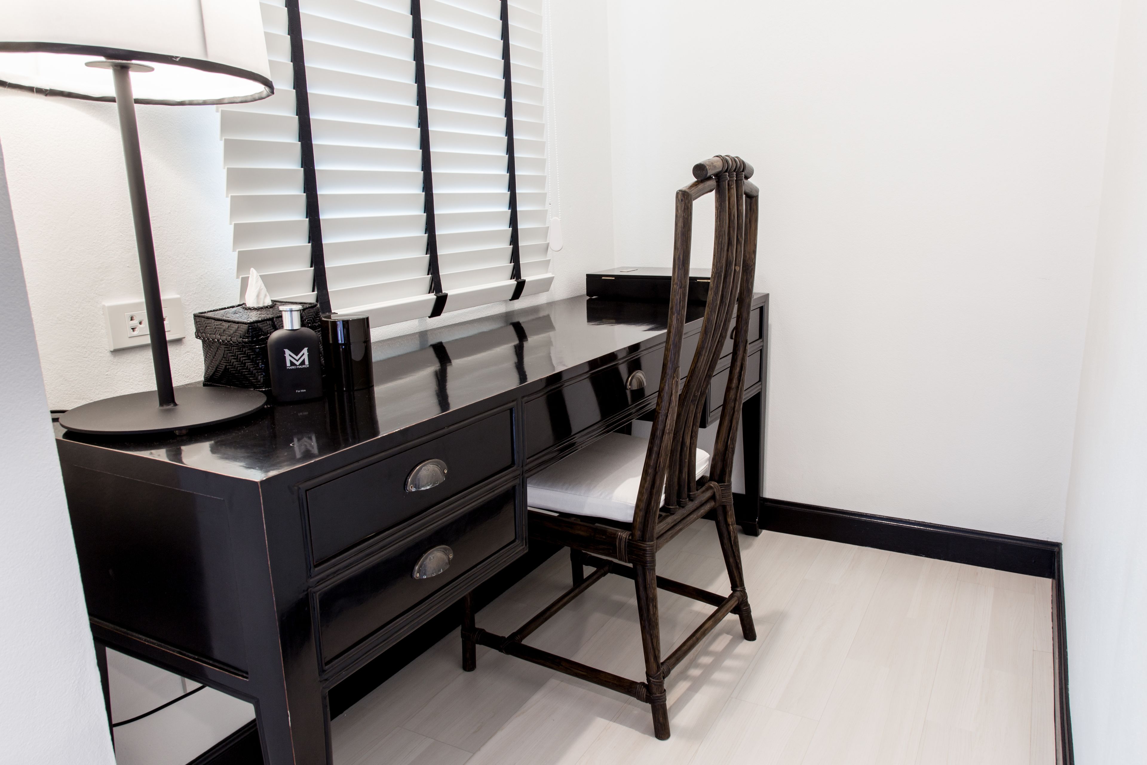 Une coiffeuse noire avec un miroir, une chaise en bois, une lampe et une boîte à mouchoirs.