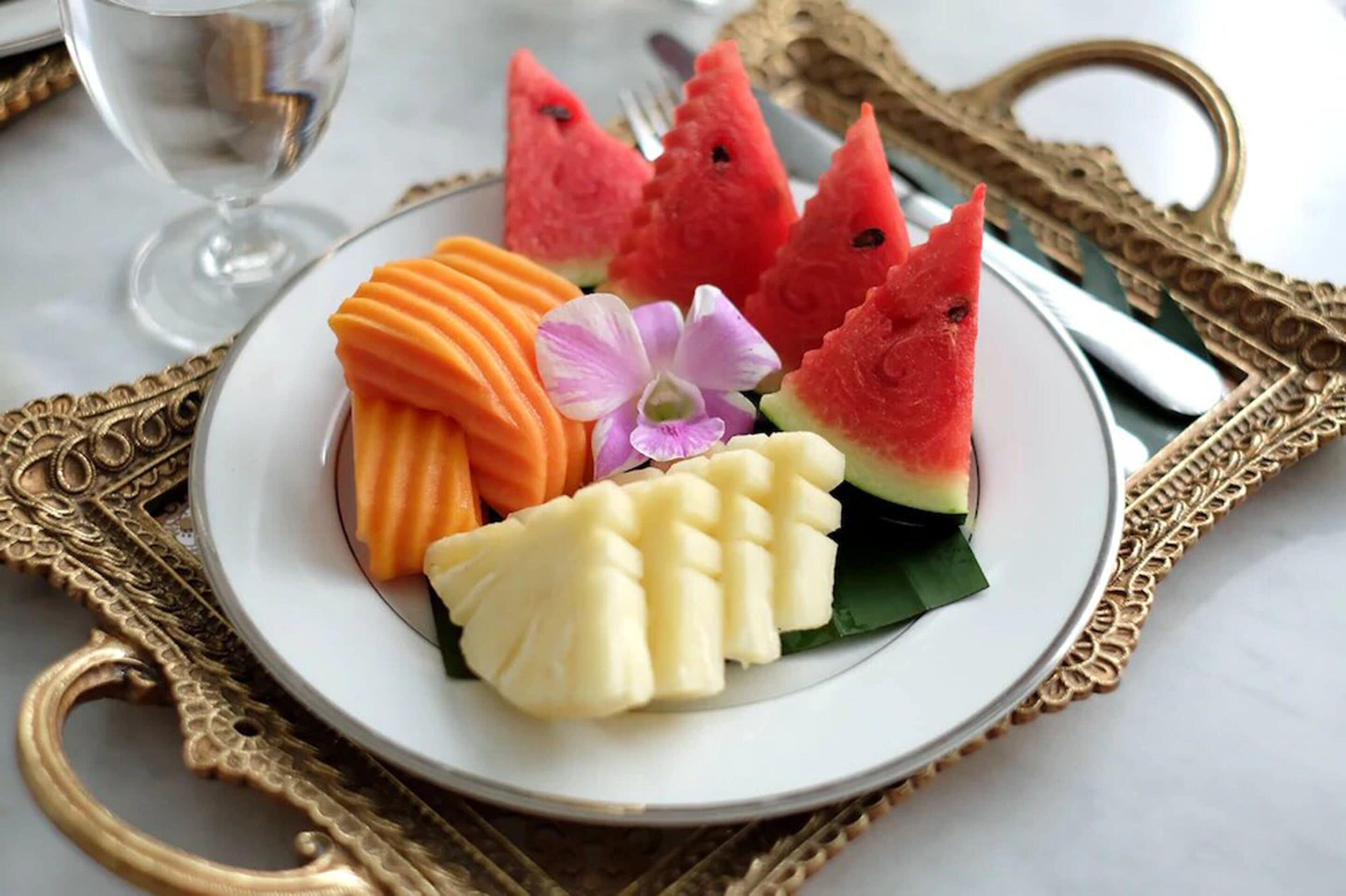 A plate with watermelon, carrot, and banana slices, accompanied by an orchid.