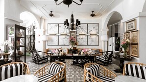 Un salon spacieux et élégamment aménagé, avec une table basse au centre, entouré de fauteuils à rayures et orné de reproductions d’plans architecturaux encadrés aux murs.