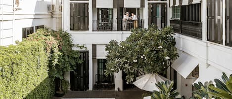 A two-story building with a swimming pool, outdoor seating, and lush greenery.