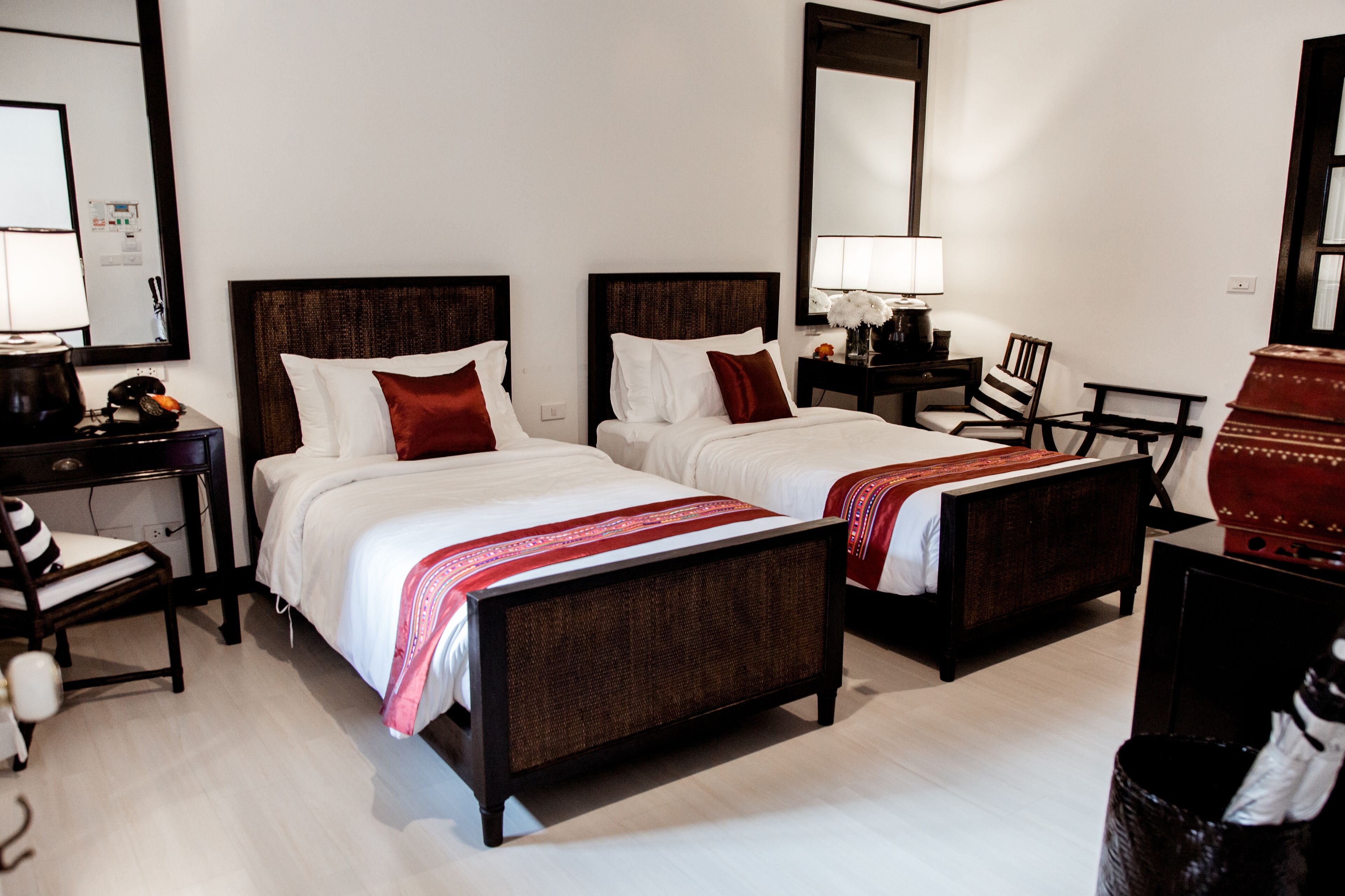 A hotel room with two beds, a desk, a chair, a lamp, and a large mirror.