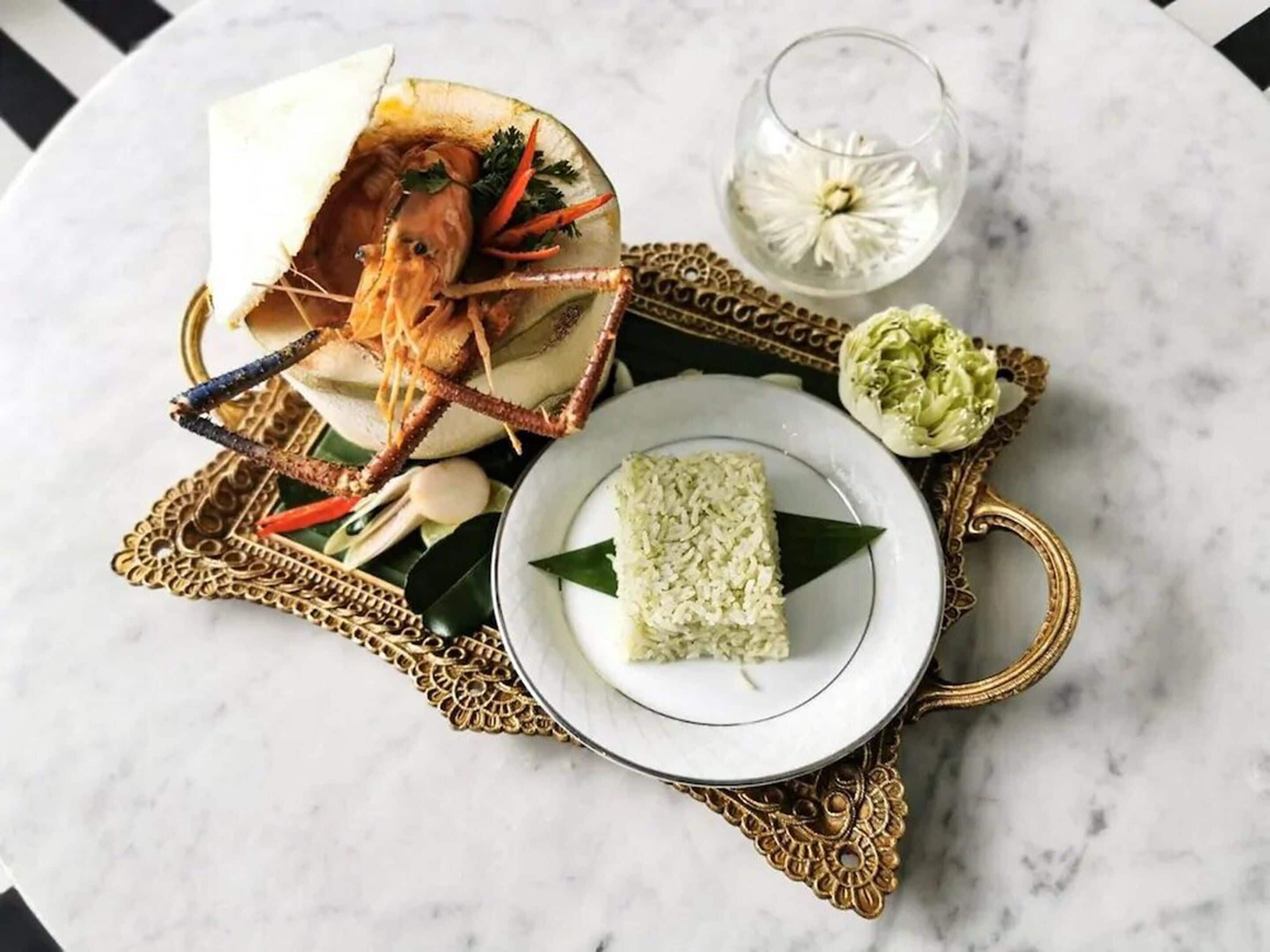 A plate of rice with a decorative leaf, a glass of water, and a decorative bowl with a seafood dish.