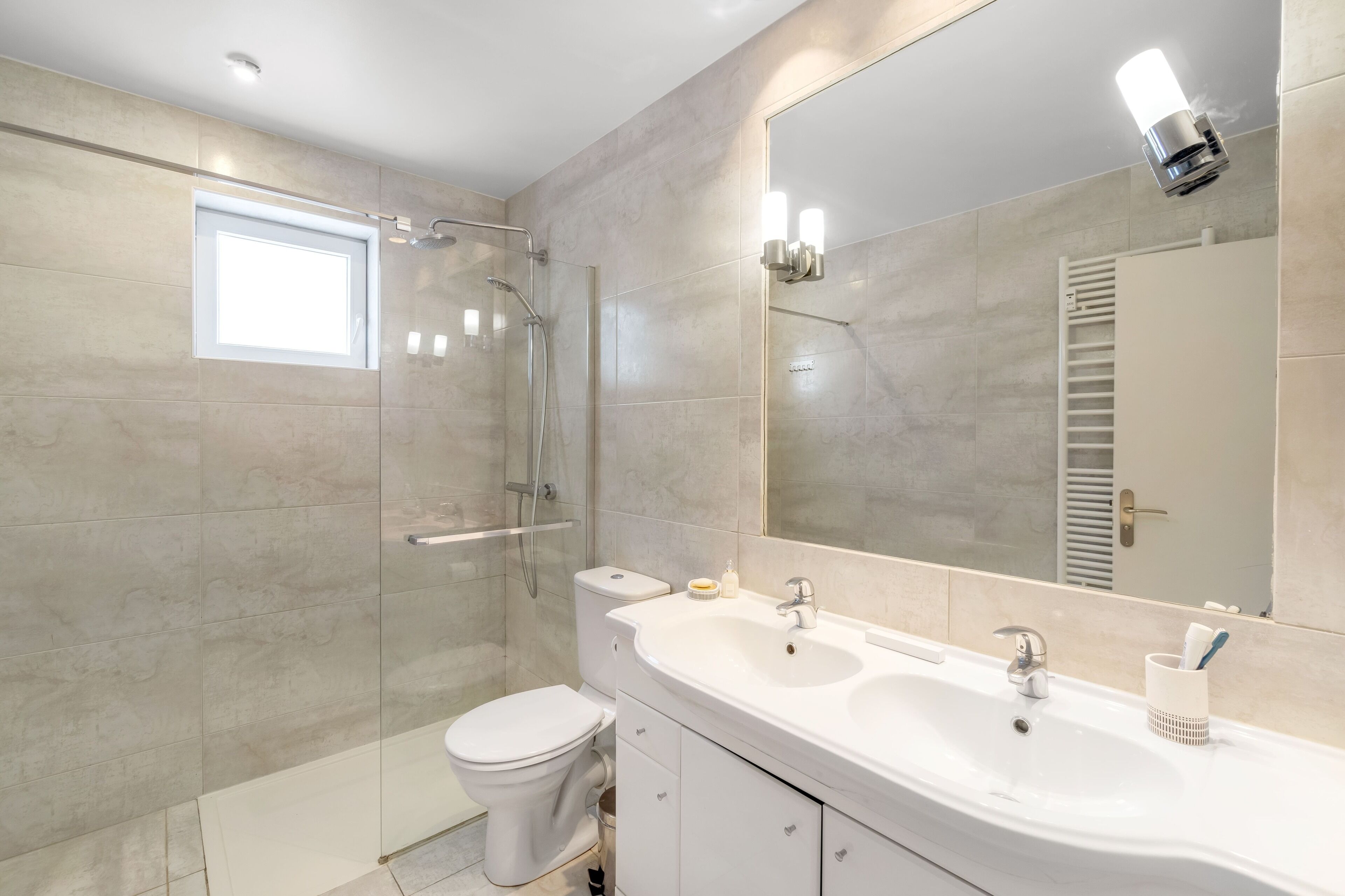Un baño moderno con cabina de ducha de vidrio, un lavabo blanco y un espejo grande.