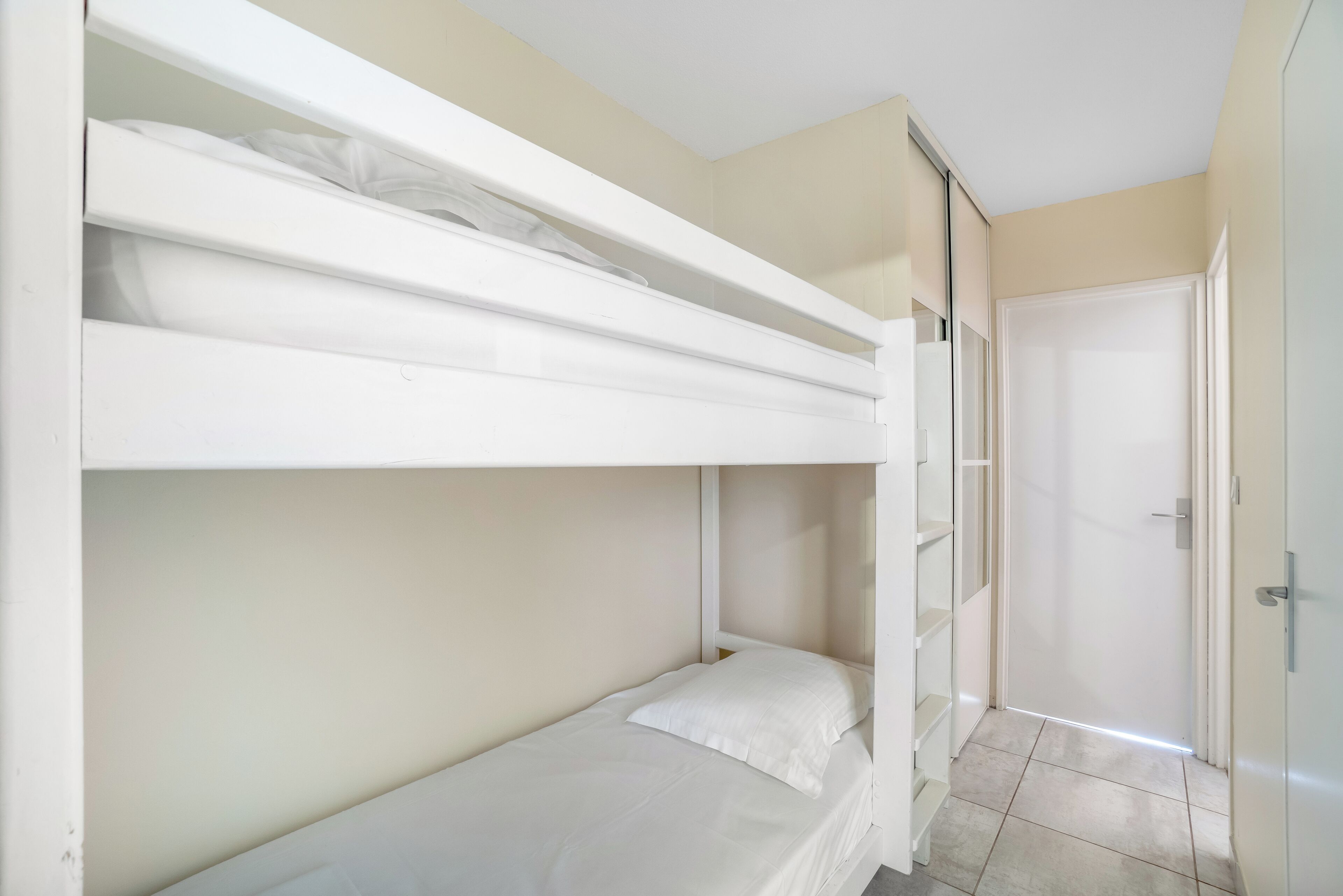 A bunk bed room with a door and a tiled floor.