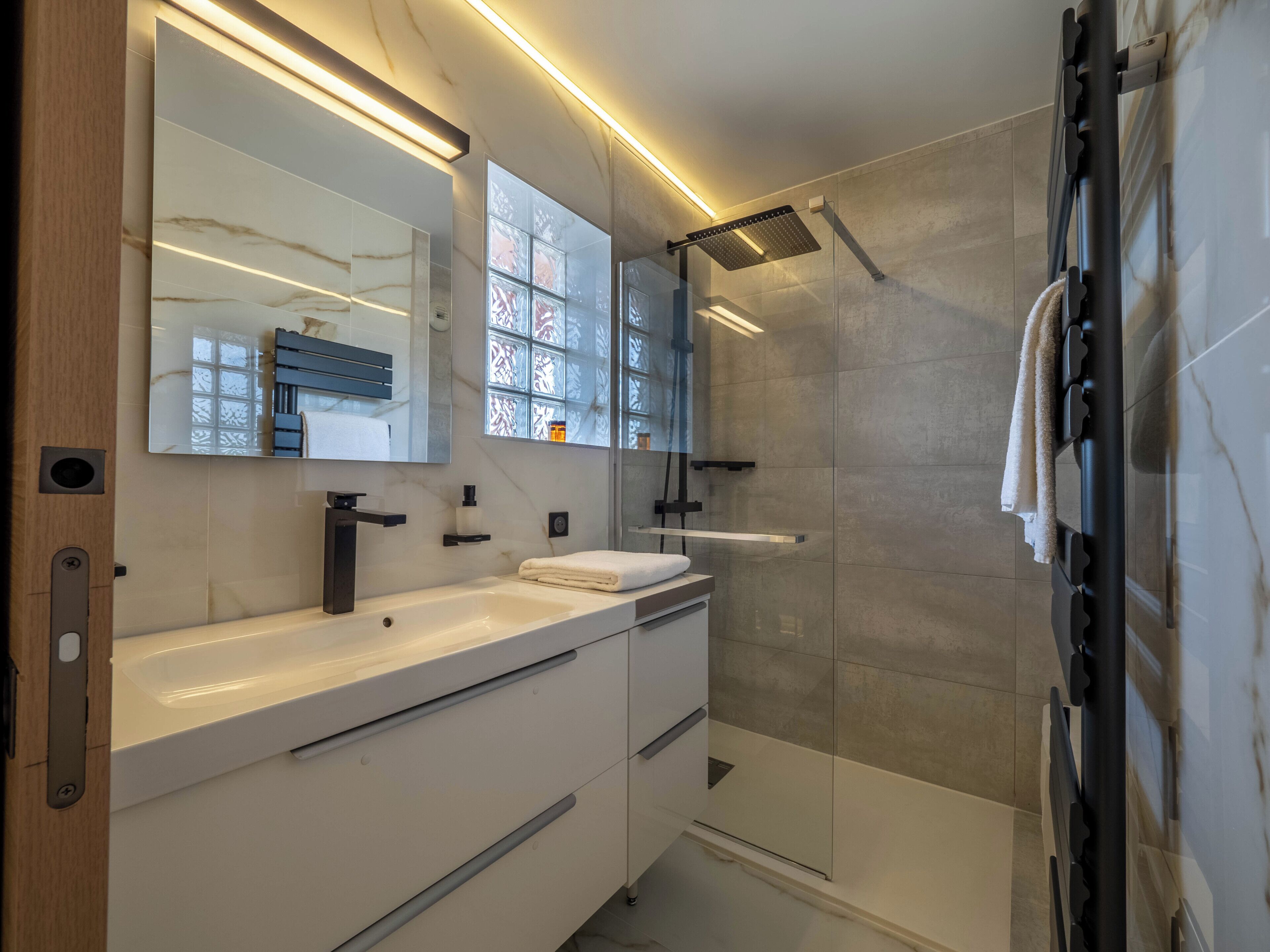 A modern bathroom with a large mirror, a white vanity, a shower area, and a towel rack.