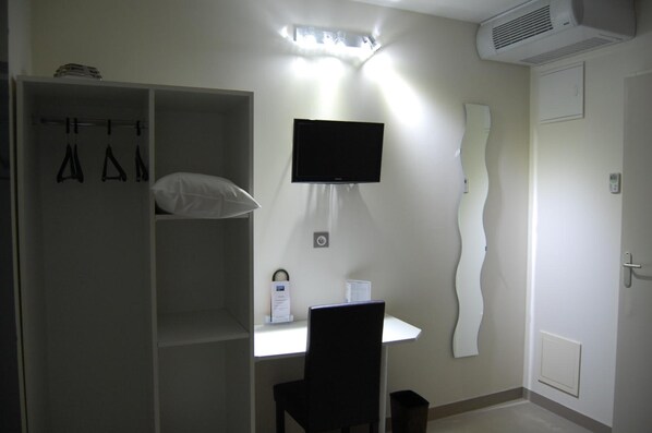Un dormitorio con escritorio, televisor, armario y espejo.