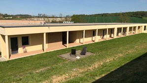 A long building with a flat roof, multiple windows, and a covered outdoor area with chairs and tables. - Hotel l Escale (Sanilhac)