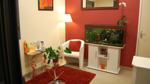 A room with a fish tank, a chair, a table with books, and a red rug. - Hotel l Escale (Sanilhac)