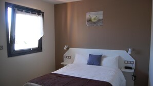 A bedroom with a bed, a window with curtains, a wall-mounted picture, and a bedside table with a phone. - Hotel l Escale (Sanilhac)