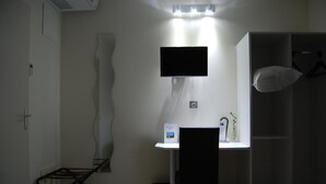 A small, dimly lit room with a single bed, a desk with a computer, and a TV mounted above it. - Hotel l Escale (Sanilhac)