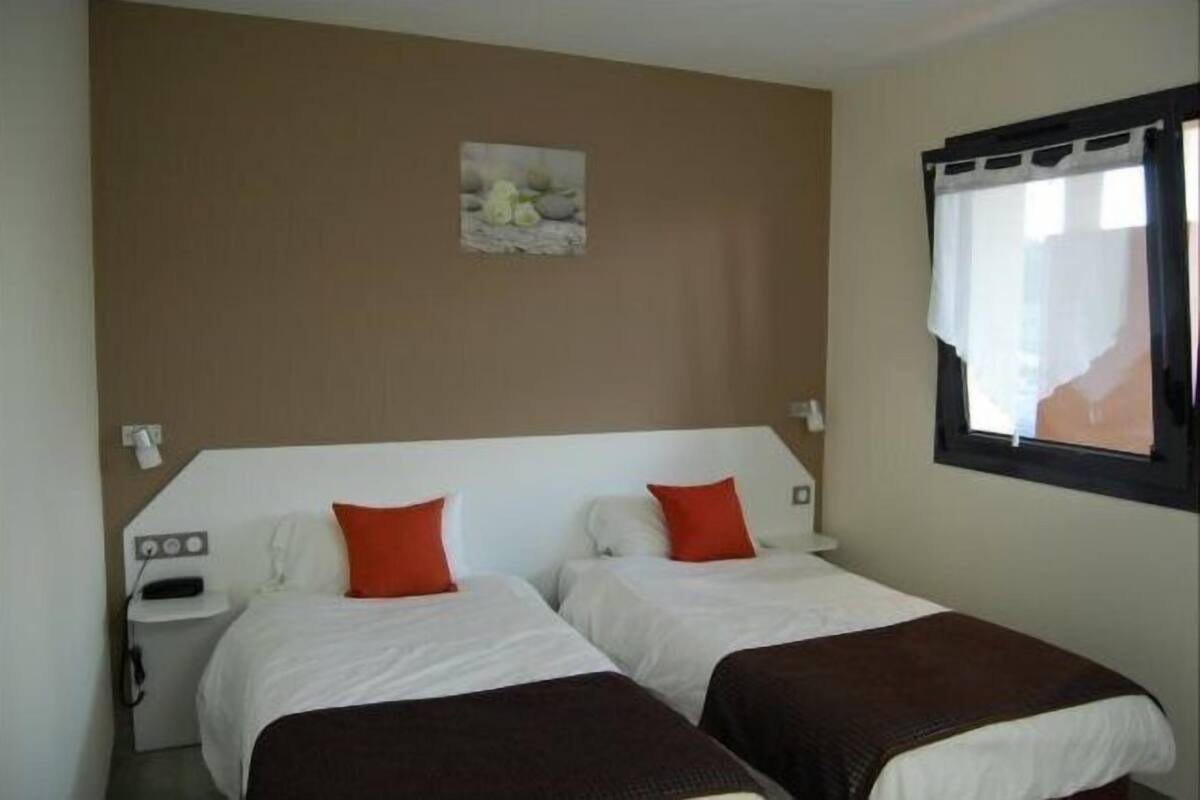 A hotel room with two beds, a small bedside table with a phone, and a window with a curtain.