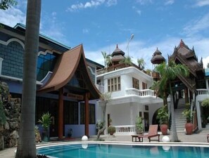 Un área de piscina con un edificio blanco, una construcción tradicional de techo curvo, y una escalera que conduce a un balcón.